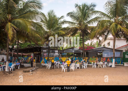 Gruppi di persone sono seduti ai tavoli lungo la spiaggia in un ristorante. Monrovia, Liberia Foto Stock