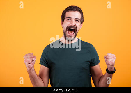 Urlando di gioia uomo eccitato con la bocca aperta da emozioni arancione su sfondo giallo. Ritratto di espressione e di fortuna Foto Stock
