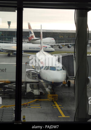 British Airways Airbus A319-100, Gate Gourmet Catering carrello e Boeing 747-400 parcheggiata con un320 rullaggio dietro al terminale5 con jetway attaccata Foto Stock