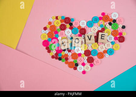 Amore parola scritta sul blocco di legno posto sul pulsante colorato a forma di cuore sul pastello colorato sfondo Foto Stock