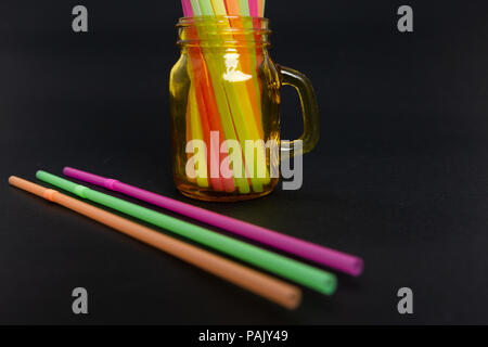 Luminose colorate party drink cannucce in vaso e i tubi in plastica ambientale monouso oggetto problema concetto su sfondo nero Foto Stock