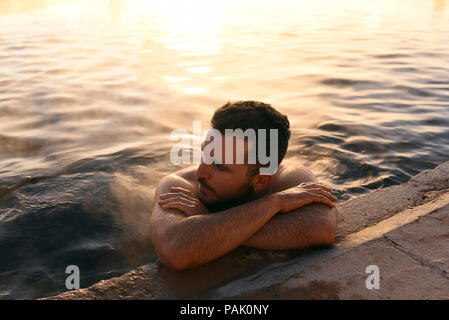 L'uomo la balneazione in hot springs con sunrise accesa il vapore in aumento in background. Termas de Polques, Sud Lípez provincia, Bolivia. Foto Stock