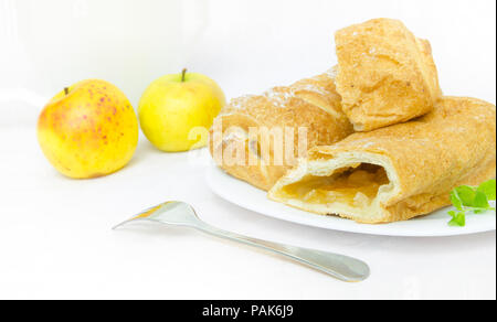 Strudel di mele su una piastra con mele fresche su sfondo bianco Foto Stock