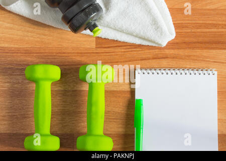 Pianificare gli allenamenti con manubri, asciugamani, acqua in bottiglia, Notepad su sfondo di legno Foto Stock