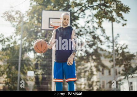 Bald attraente uomo giocare a basket sul campo da basket. L uomo è sul fuoco e primo piano, Basketball hoop e la scheda sul background e blurre Foto Stock