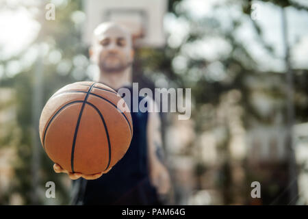 Close up di bald attraente uomo holding basket. La sfera è sul fuoco e primo piano. L'uomo, Basketball hoop e la scheda sullo sfondo e sfocata. Foto Stock