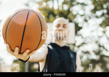 Close up di bald attraente uomo holding basket. La sfera è sul fuoco e primo piano. L'uomo, Basketball hoop e la scheda sullo sfondo e sfocata. Foto Stock