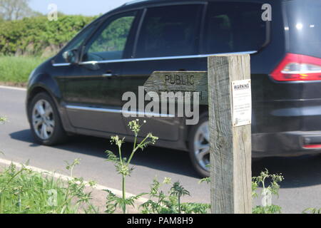 Dito di legno segno che indica un sentiero pubblico lungo il lato di una strada con il passaggio di un auto da Foto Stock