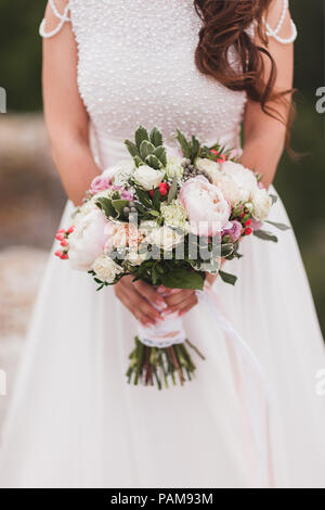 Sposa tenendo nelle mani di bouquet di fiori in stile classico con peonia e nastri di seta bianca Foto Stock