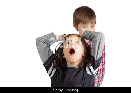 Un piccolo fratello tira i capelli di sua sorella. Egli guarda sly e maliziosa. Lei afferra la testa con una bocca aperta cercare di shock e dolore. Foto Stock