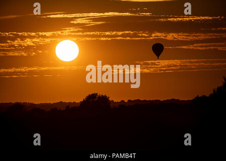Una mongolfiera galleggia sopra la campagna del Wiltshire come il sole tramonta sul il giorno più caldo dell'anno nel Regno Unito. Foto Stock