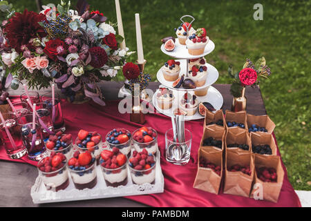 Freschi e saporiti i tortini con bacche sul ricevimento di nozze tabella, decorate in colore rosso con fiori Foto Stock
