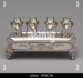 Inkstand. Cultura: British, Londra. Dimensioni: Larghezza: 13 3/16 in. (33,5 cm). Autore: John Plimmer (attivo 1771-1803). Data: 1802. Il inkstand ha quattro a forma di vaso contenitori supportati in telai per treppiede che suggeriscono in miniatura, le gabbie di antichità che gli europei chiamato 'Atheniennes". Due dei contenitori hanno fori nei coperchi per penne e inchiostri e un terzo ha un design forato sul coperchio per sabbia, che serviva per asciugare l'inchiostro. Il quarto contenitore tenutasi probabilmente wafer--Piccola readymade incolla-dischi per la sigillatura di lettere. Vi è una profonda scanalatura su ciascuno dei lati lunghi per penne e un vassoio Foto Stock