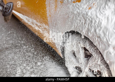White Shampoo schiuma spruzzata su auto ruota posteriore e laterale, quando lavato in autolavaggi. Foto Stock