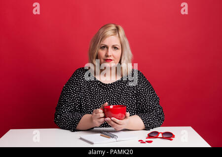 Ritratto di un attraente Donna sovrappeso in studio su uno sfondo di colore rosso. Foto Stock