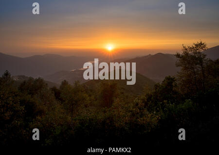 Impostazione di colore arancione sun immersione al di sotto di uno strato di smoky wildfire haze - Guardando ad ovest sulla Sierra Foothills dal sacerdote strada di grado in montagna. Foto Stock