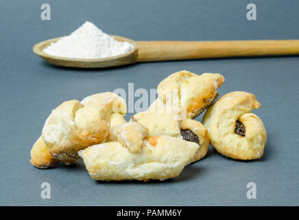 Mezzaluna tradizionali panini con marmellata di prugne e un cucchiaio di legno con la farina su uno sfondo grigio Foto Stock