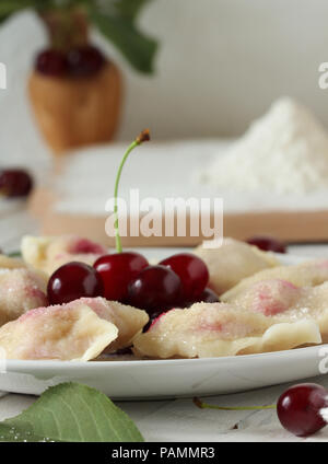Vareniki (pierogi) con ciliegie su un bianco sullo sfondo di legno - Ucraina piatto nazionale Foto Stock