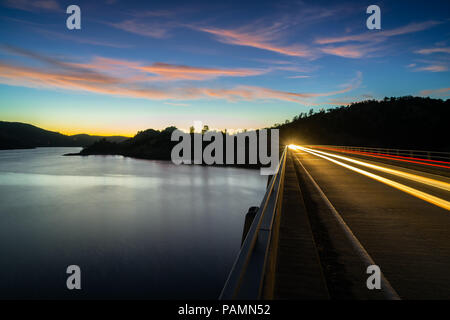 Nuvole rosa e sentieri dei fari sopra l'acqua liscia di Don Pedro il serbatoio e il lago, Sierra Foothills - Tuolumne County, California Foto Stock