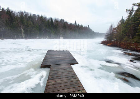Dock su un lago ghiacciato con la nebbia, nel nord del Québec in Canada. Il lago è circondato da abeti e abeti. Foto Stock
