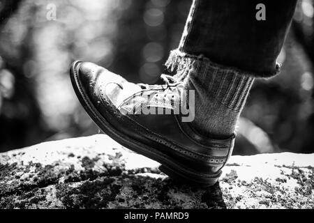 Piede maschile di indossare scarpe di cuoio, in piedi su una roccia con una natura sfondo sfocato, in bianco e nero Foto Stock