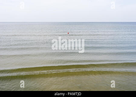 Red boa galleggiante sul mare in calmo con una singola onda sullo sfondo di un cielo senza nuvole Foto Stock