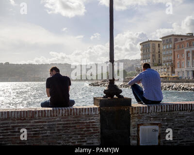 Gli uomini seduti sulla strada rialzata che conduce al Castel dell'Ovo a Napoli, Italia. Foto Stock