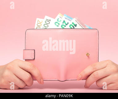 Borsa rosa e le banconote in euro in mani femminili su sfondo rosa. Il concetto di business. Foto Stock