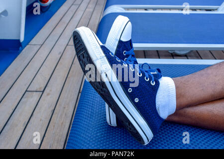 Il relax. Piedini maschio incrociati, indossando sneakers blu, in poltrona. Foto Stock