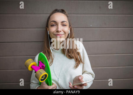 Ritratto di sorridente ragazza adolescente con un telefono cellulare, auricolari e skateboard Foto Stock