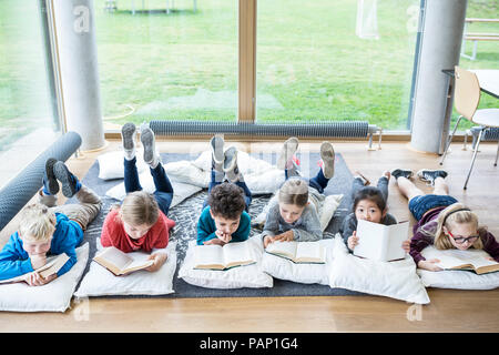 Gli alunni sdraiato sul pavimento la lettura di libri di scuola sala pausa Foto Stock