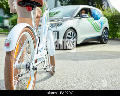 Donna con la bicicletta nella parte anteriore della macchina elettrica Foto Stock