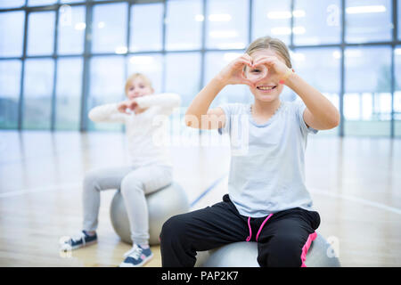 Ritratto di sorridere studentesse seduti sulla palla in palestra classe Foto Stock