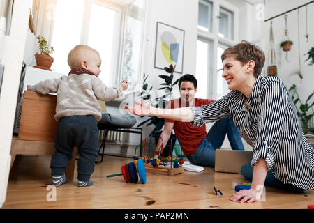 La famiglia felice seduto a terra, playinhg con la loro figlia piccola Foto Stock