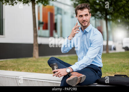 Imprenditore sorridente seduti all'aperto con un telefono cellulare e il caffè da asporto Foto Stock