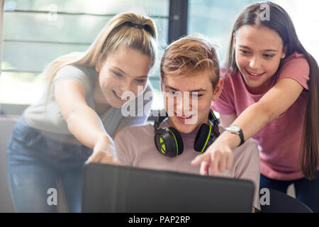 Le ragazze adolescenti guardando boy utilizzando laptop Foto Stock