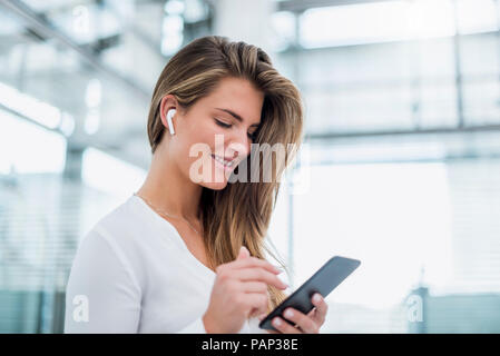 Sorridente giovane donna indossa in-ear telefono tramite telefono cellulare Foto Stock
