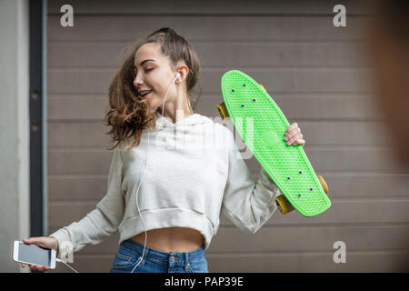 Carefree ragazza adolescente ballare tenendo skateboard e ascolto di musica Foto Stock