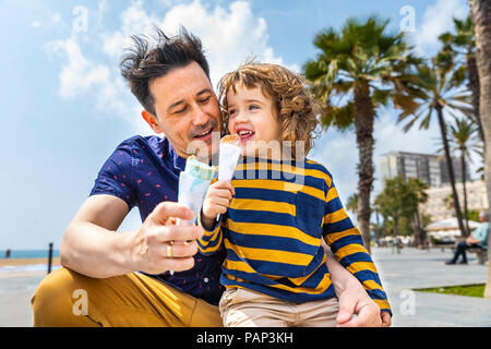 Spagna, Barcellona, padre e figlio godendo di un gelato al mare Foto Stock