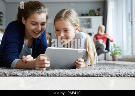 Teo sorelle sdraiato sul pavimento, giocando con tavoletta digitale Foto Stock