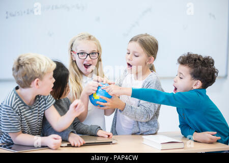 Felice gli alunni holding globe insieme in classe Foto Stock
