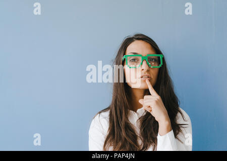 Giovane donna che indossa gli occhiali di pixel, mettendo il dito sulla bocca Foto Stock