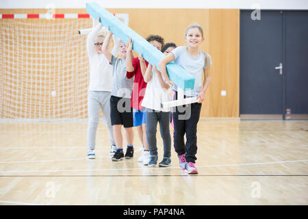 Gli alunni che trasportano il fascio di equilibrio nella palestra di classe Foto Stock