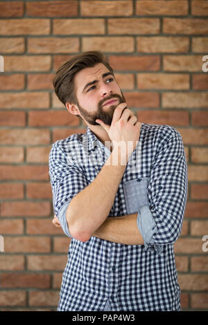 Ritratto di barbuto giovane uomo di fronte a un muro di mattoni di pensare Foto Stock