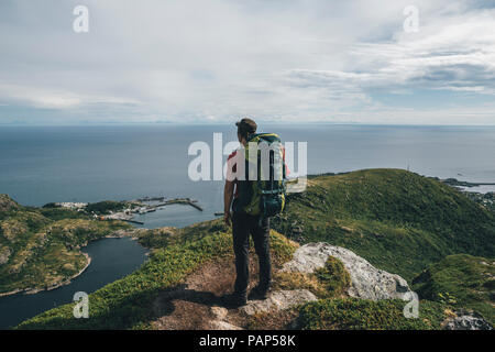 Norvegia, Lofoten, Moskenesoy, Backpacker permanente sulla scogliera, guardando all'Oceano Atlantico Foto Stock