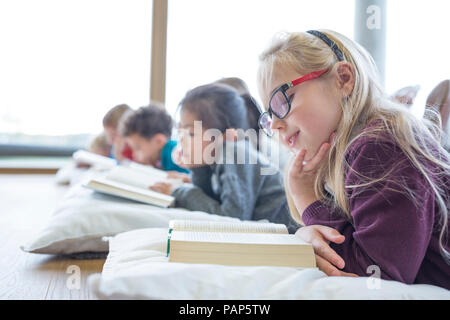 Gli alunni sdraiato sul pavimento la lettura di libri di scuola sala pausa Foto Stock