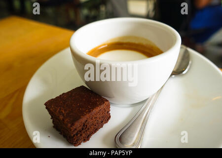 Piastra, cup, e cucchiaio che accompagnano un italiano di latte e torta al cioccolato in Singapore Foto Stock