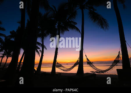 Amaca sagome tra palme in riva al mare sulla spiaggia, con splendide, coloratissima isola Sunrise - Bohol, Filippine Foto Stock