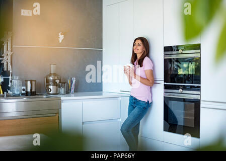 Donna sorridente a casa in cucina con la tazza di caffè Foto Stock