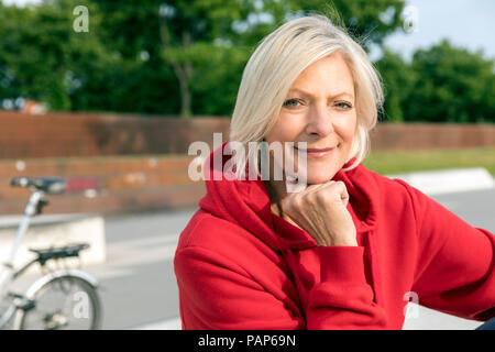 Ritratto di sorridere senior donna che indossa felpa con cappuccio rosso all'aperto Foto Stock